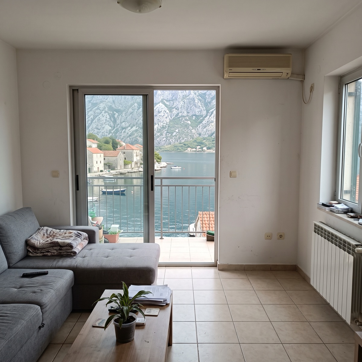 Living room of an apartment in Dobrota with an open balcony door and a view over the Bay of Kotor to the mountains.